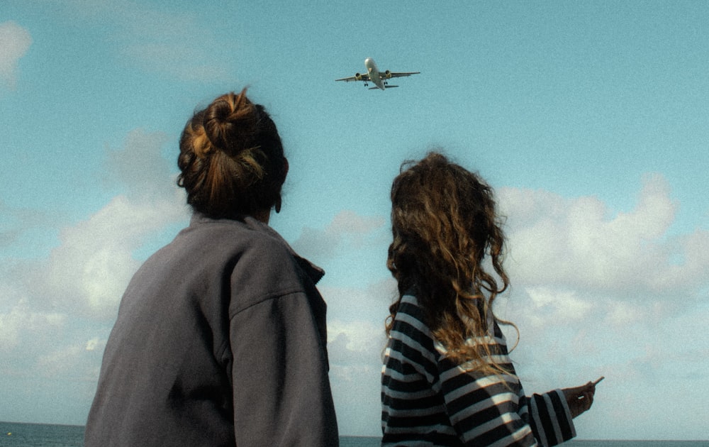 two people looking at an airplane in the sky