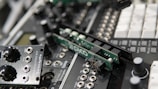 A close-up of electronic audio equipment featuring several modular synthesizer components, including circuit boards and knobs with various labels. The details highlight connectors, switches, and various controls for sound modulation.