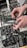 Hands are adjusting black electronic modules with various knobs and ports. The modules are part of a more extensive setup of electronic equipment, possibly a modular synthesizer, featuring various buttons and inputs.