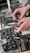 Hands are adjusting black electronic modules with various knobs and ports. The modules are part of a more extensive setup of electronic equipment, possibly a modular synthesizer, featuring various buttons and inputs.
