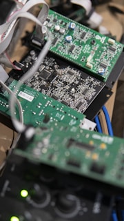 Several green circuit boards with various electronic components such as resistors, capacitors, and integrated circuits. Ribbon cables connect the boards, and blue cables are visible in the background.