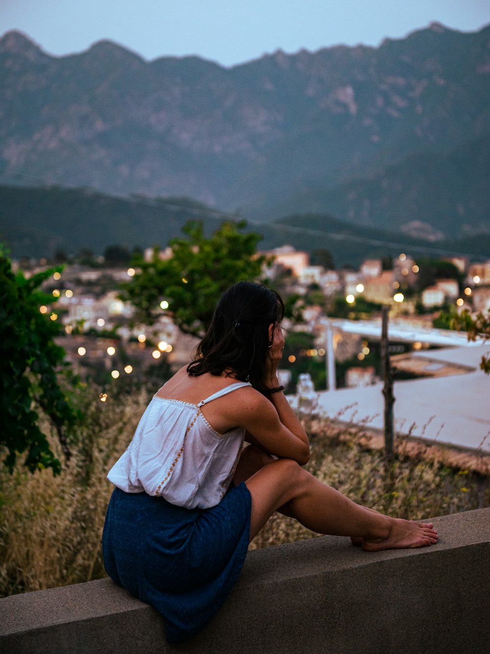 a woman sitting on a ledge looking at the city