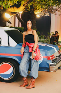 Evening scene of a plus-size model wearing the ‘V8 Muscle’ graphic sweatshirt, leaning on the hood of a black muscle car under neon lights.