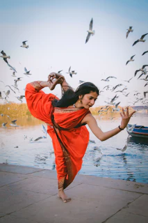 a woman in a red dress is dancing near a body of water
