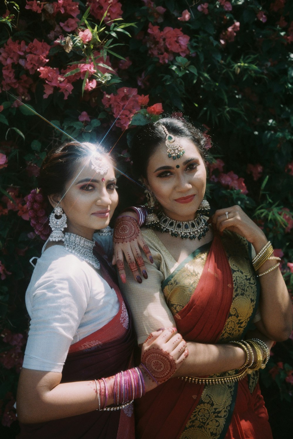 two women standing next to each other in front of flowers