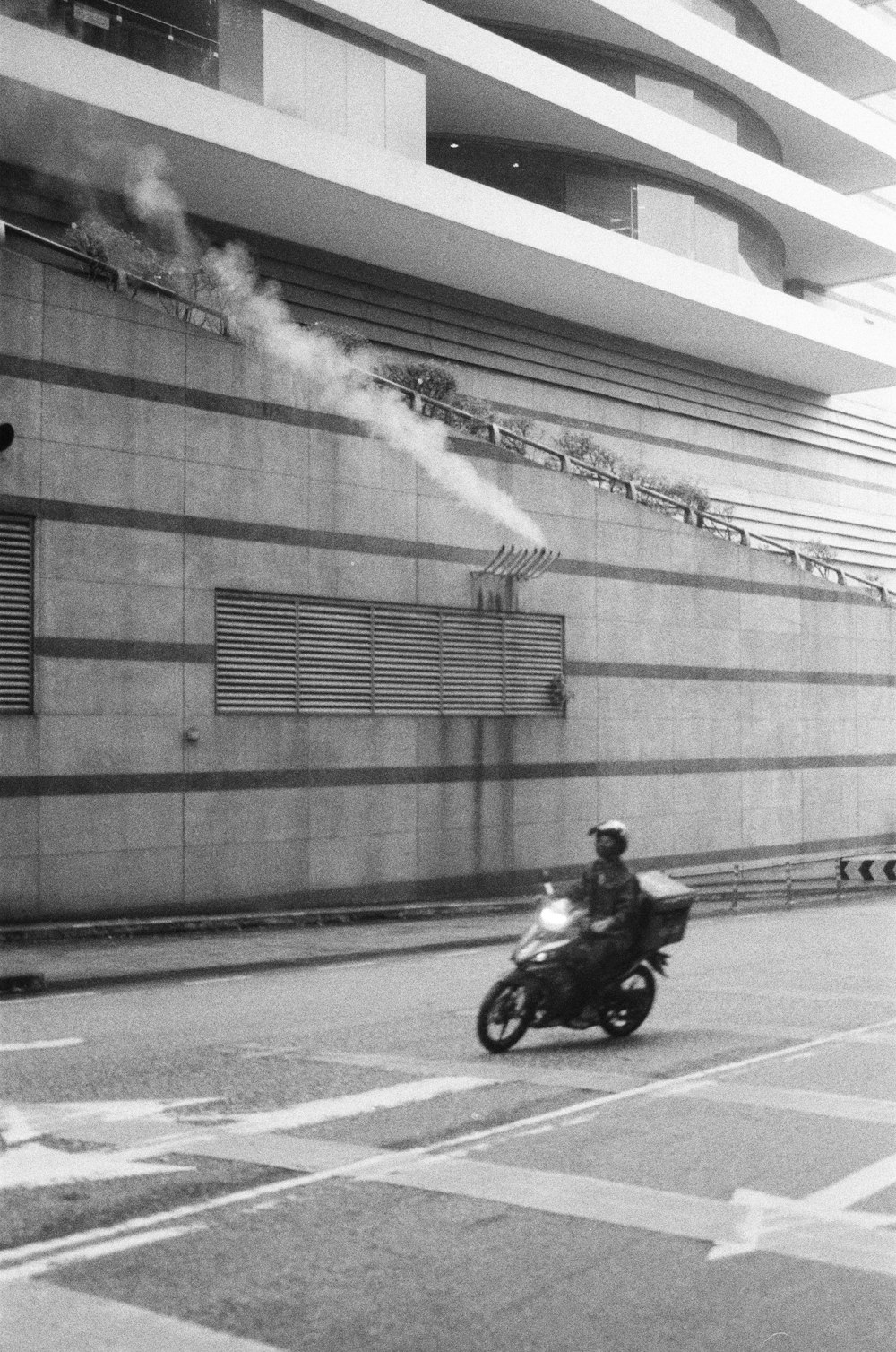 a man riding a motorcycle down a street next to a tall building