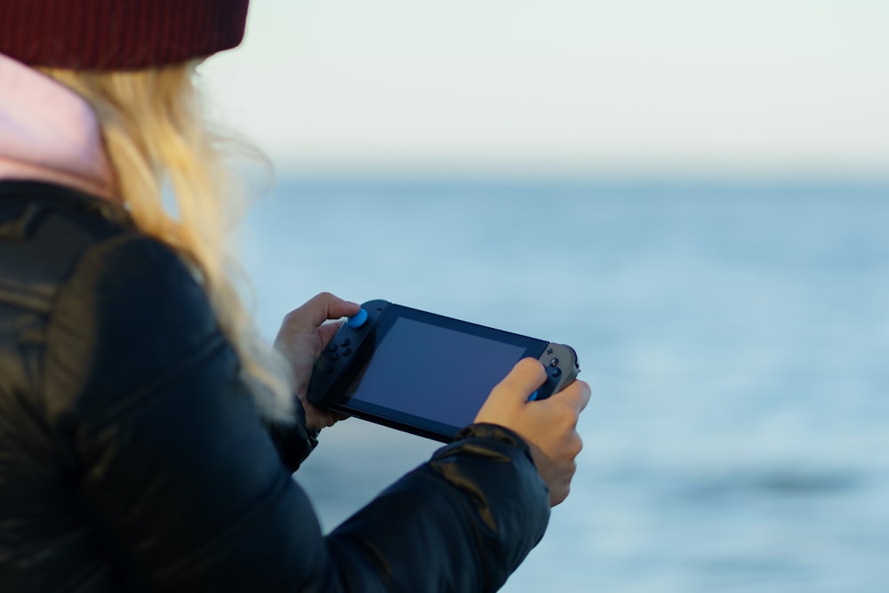 uma mulher segurando um controlador de jogo na frente de um corpo de água