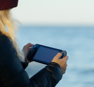 a woman holding a game controller in front of a body of water