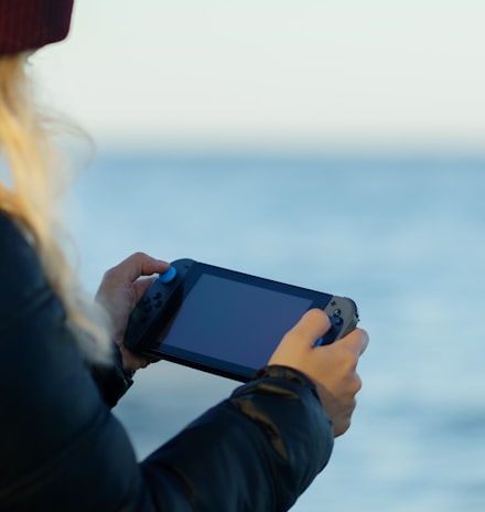 a woman holding a game controller in front of a body of water