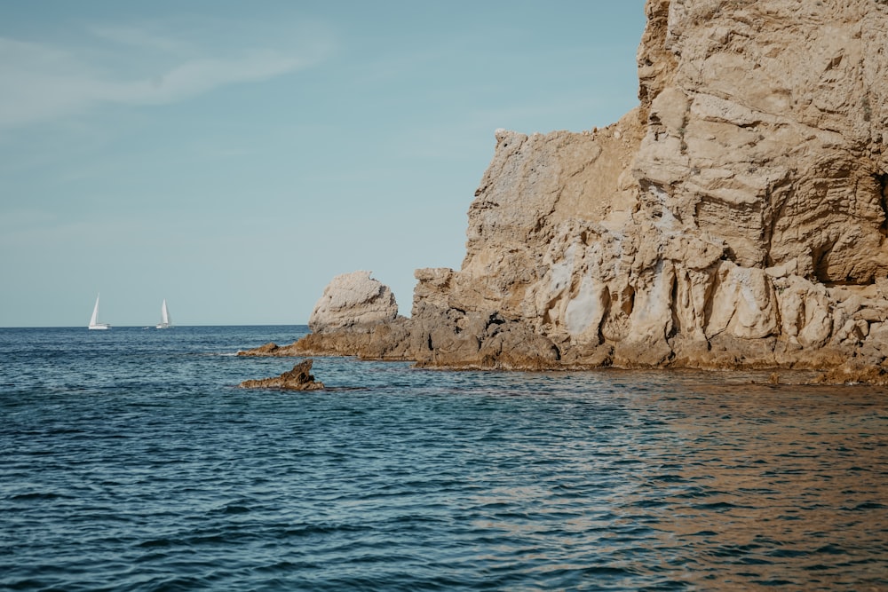 a sailboat is in the water near a rocky cliff