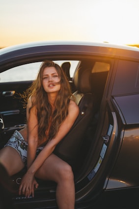 A friendly female driver helping a senior woman into a clean, comfortable vehicle at sunset.
