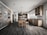 A modern kitchen with sleek wooden cabinetry and stainless steel appliances. The room features a center island with stools, a hanging light fixture, and ample natural light from large windows. Shelving displays various food and beverage items.