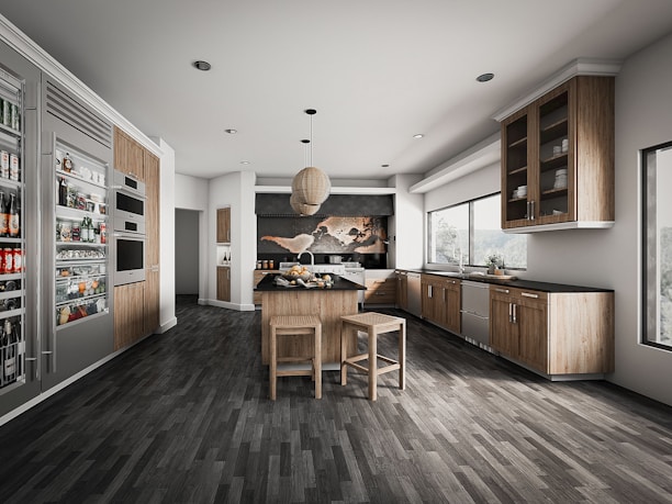 A modern kitchen with sleek wooden cabinetry and stainless steel appliances. The room features a center island with stools, a hanging light fixture, and ample natural light from large windows. Shelving displays various food and beverage items.