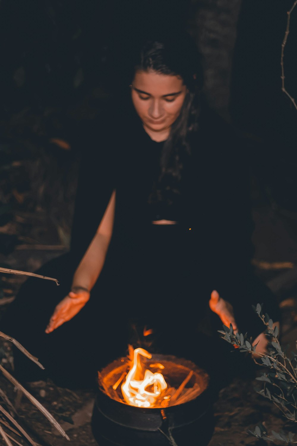 a woman sitting on the ground in front of a fire