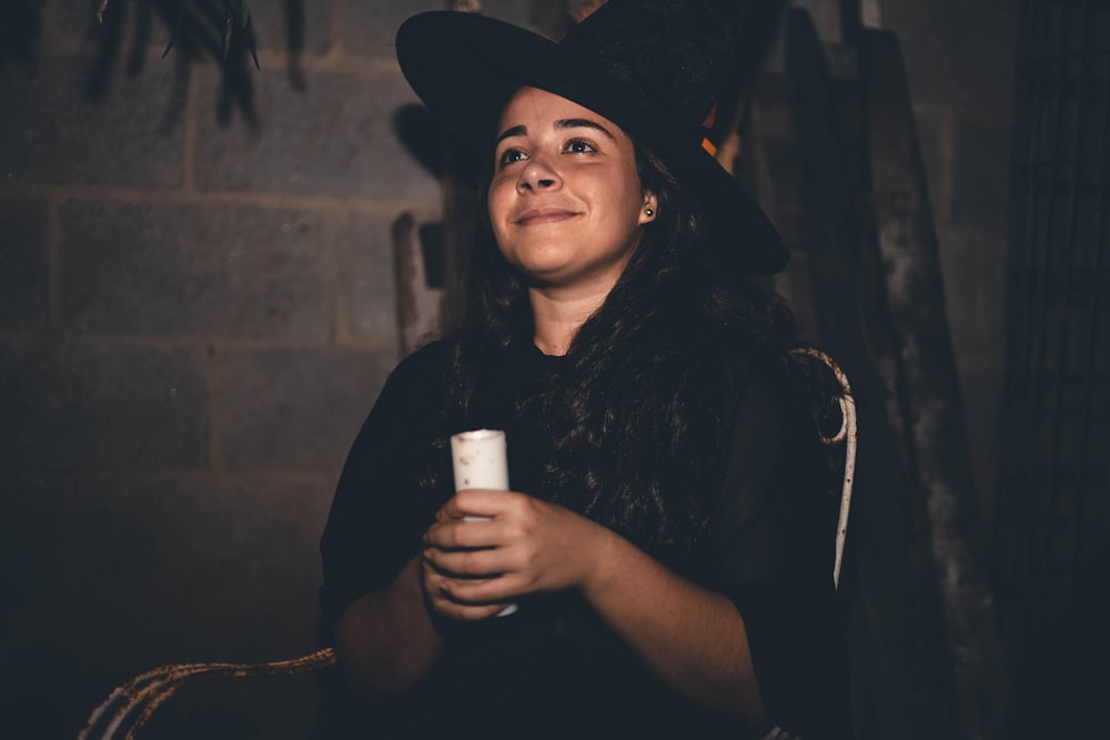 a woman wearing a black hat and holding a cup