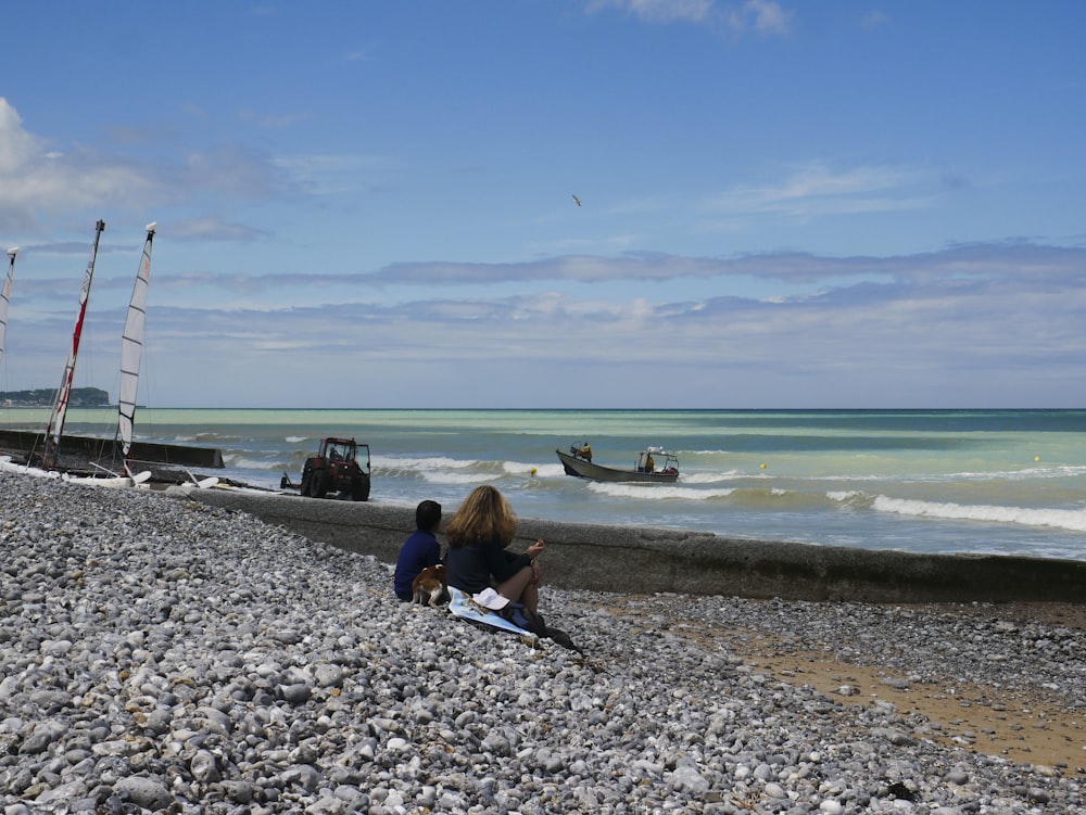 a couple of people sitting on top of a rocky beach