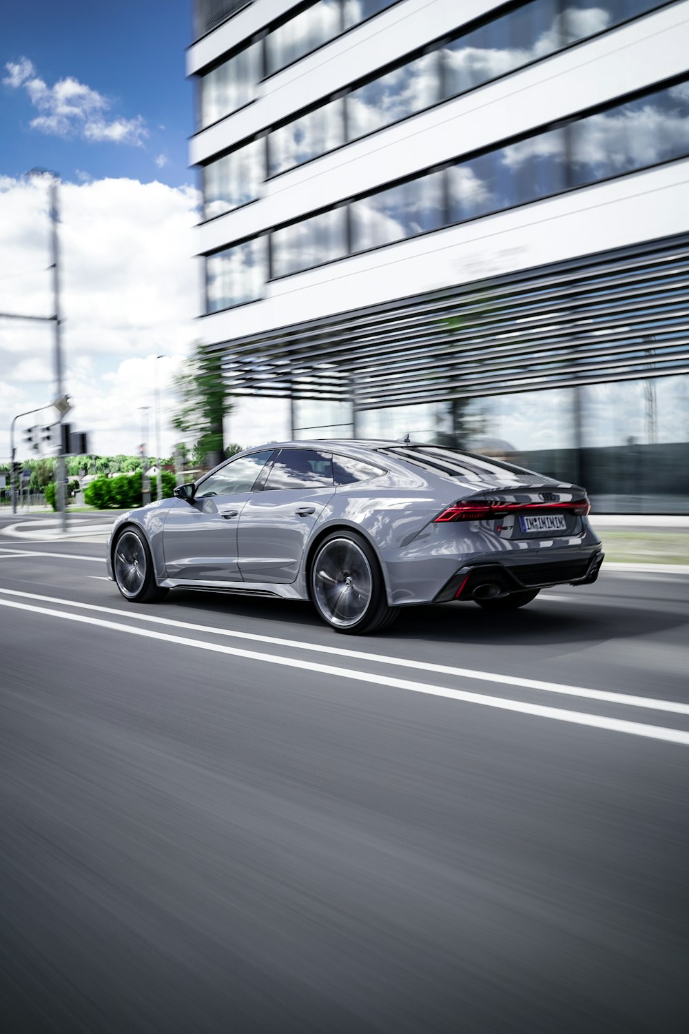 a silver car driving down a street next to a tall building