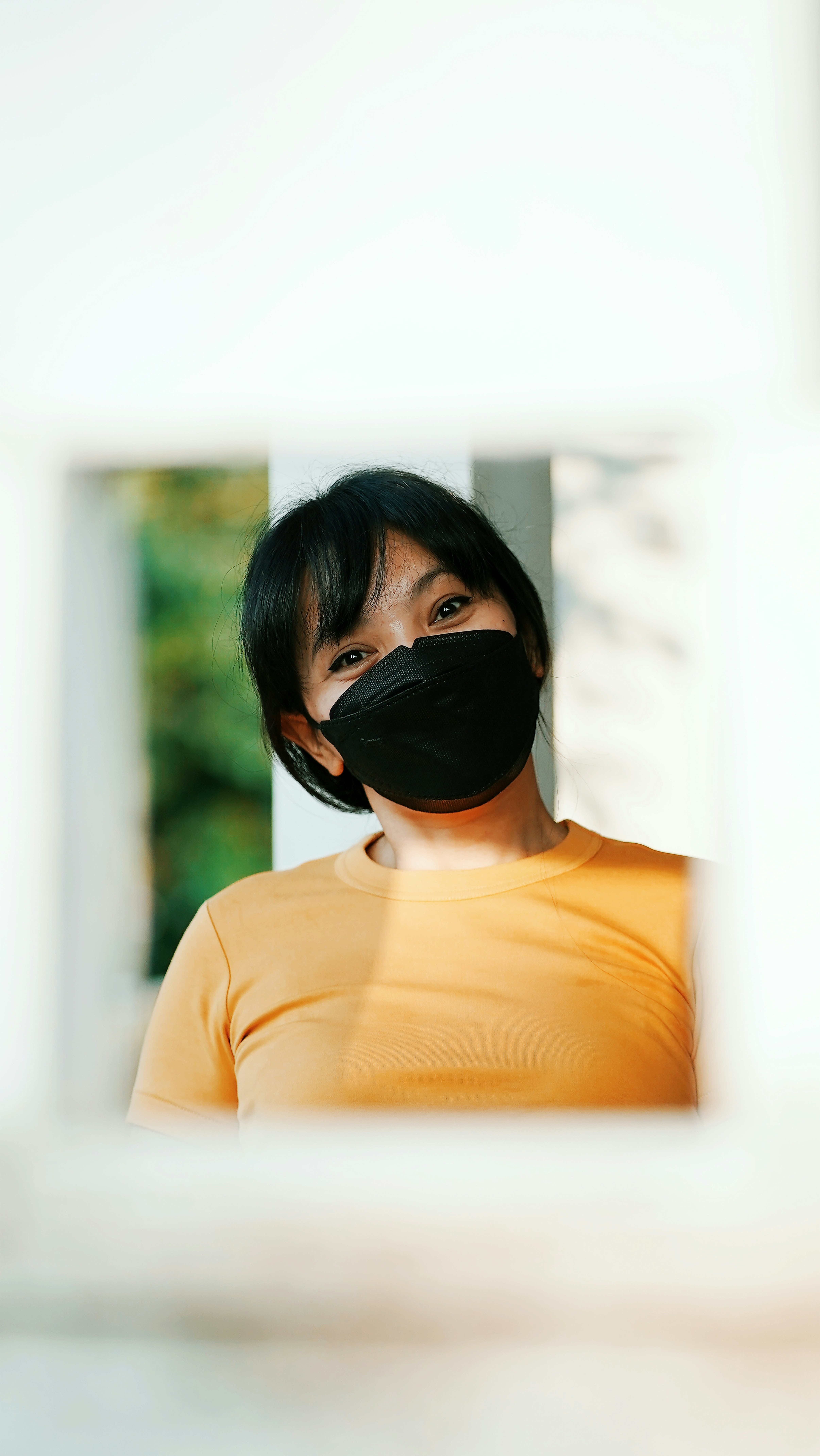 a woman wearing a black face mask looking out a window