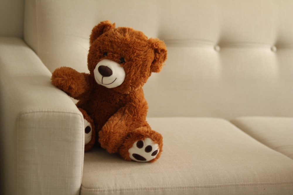 a brown teddy bear sitting on a white couch