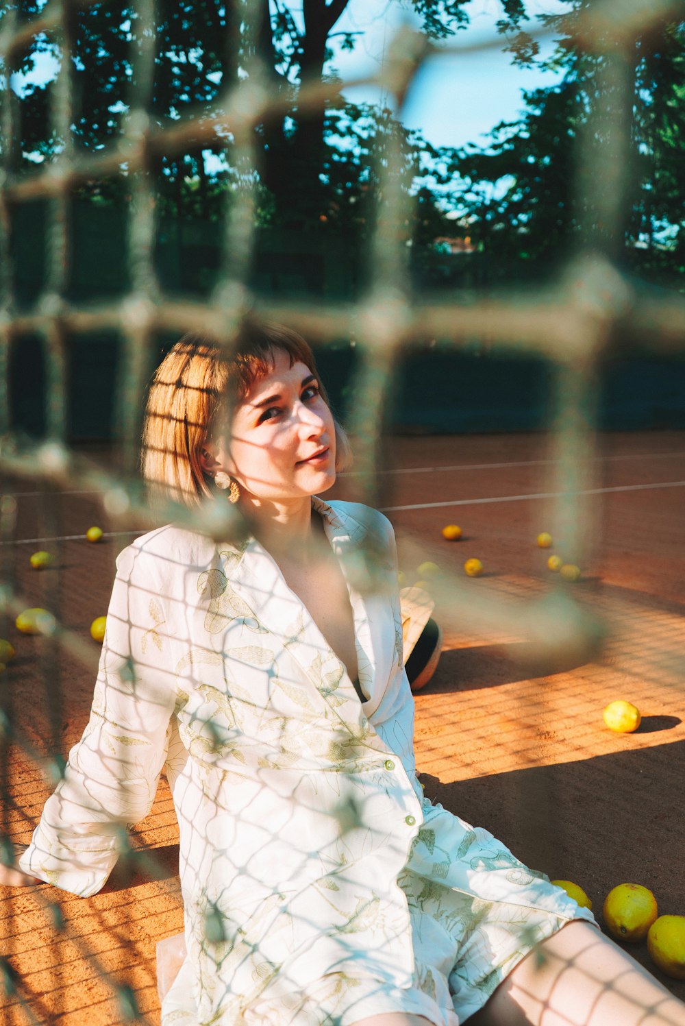 Eine Frau im weißen Kleid sitzt auf einem Tennisplatz