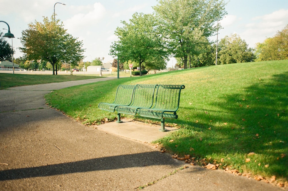 a green park bench sitting on top of a sidewalk