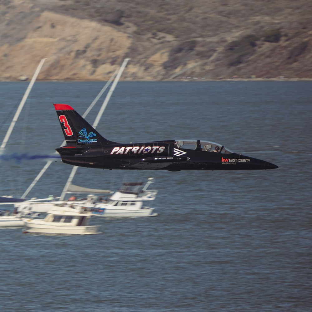 a black jet flying over a body of water