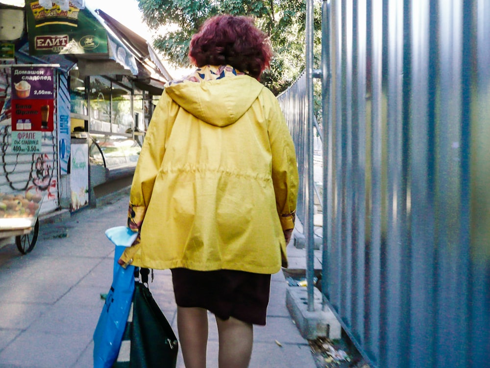 a woman in a yellow jacket walking down a sidewalk
