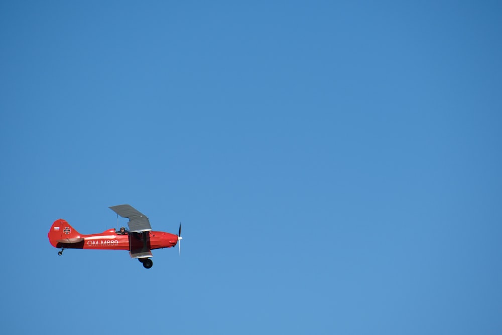a small red airplane flying through a blue sky