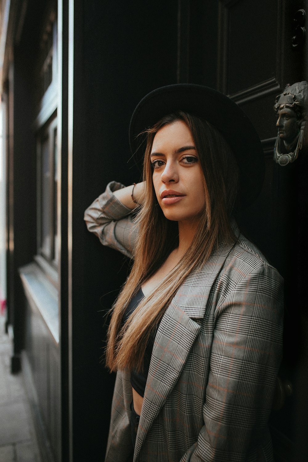 a woman in a suit and hat leaning against a door