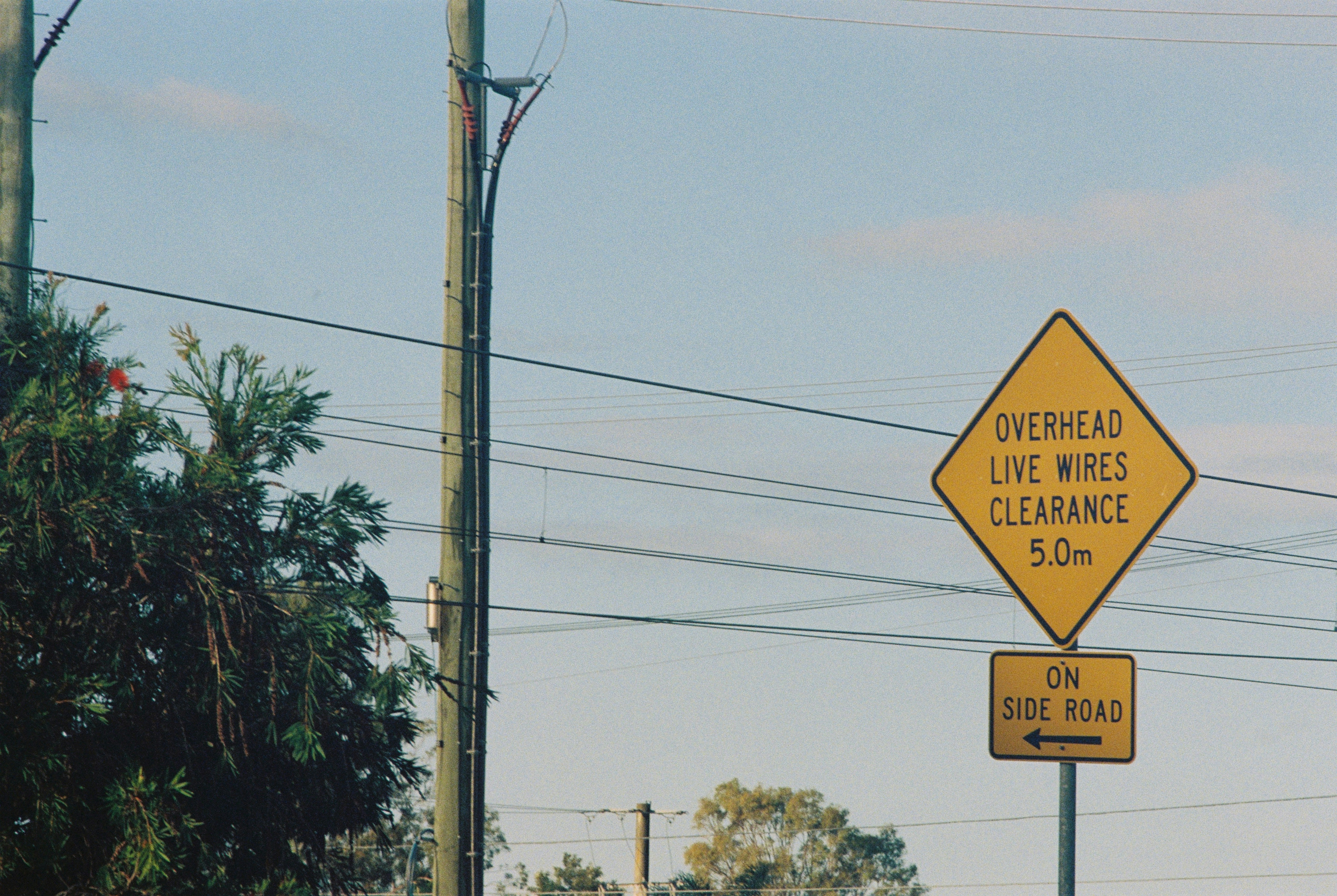 A yellow diamond-shaped sign warning of overhead live wires with a 5.0m clearance, essential traffic cautionary signs for high-clearance vehicles.