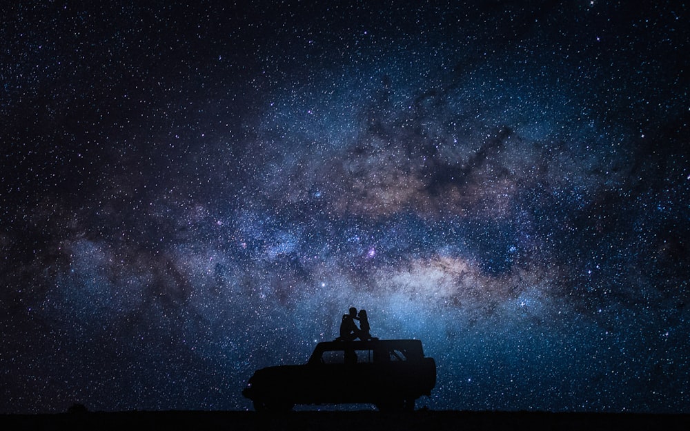 two people sitting on the roof of a truck under a night sky filled with stars