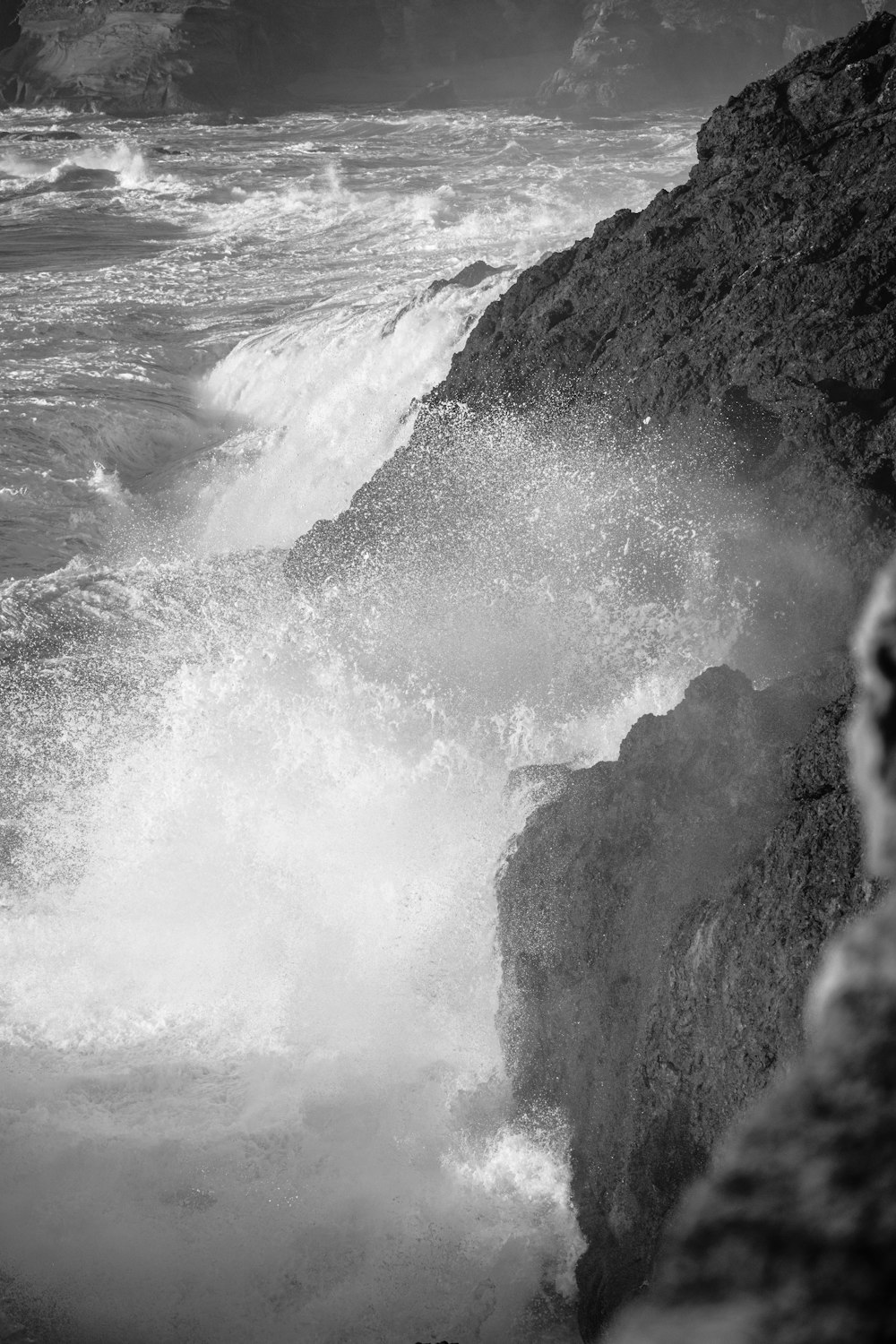 a black and white photo of a wave crashing against a rock