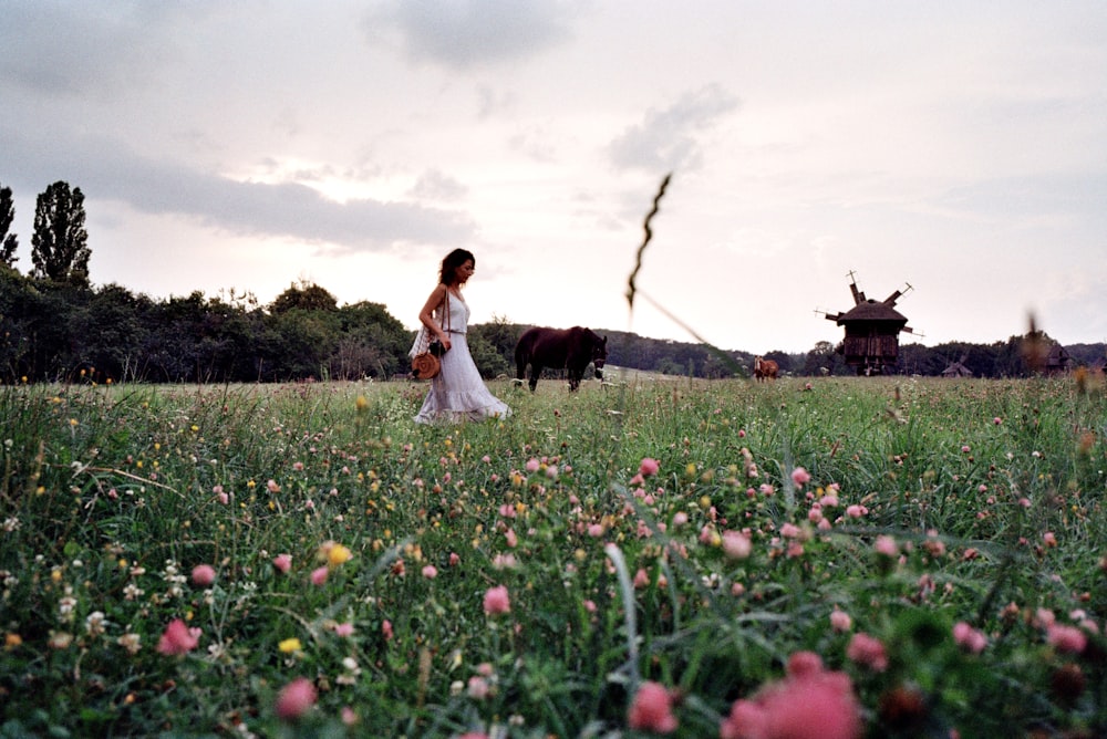 uma mulher em um vestido branco em pé em um campo com um cavalo