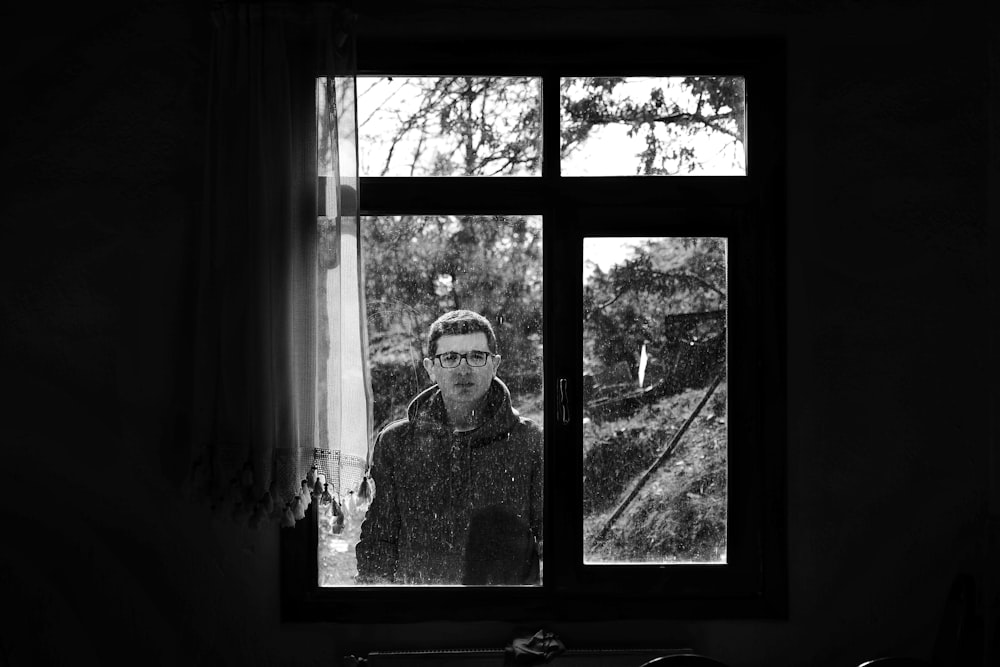 a black and white photo of a man looking out a window