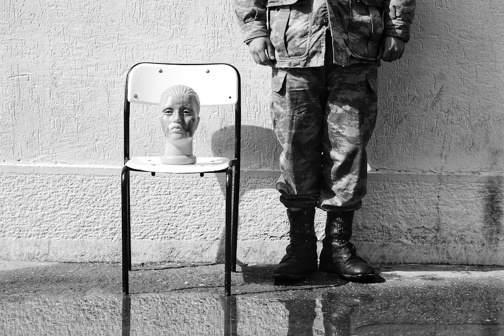 a black and white photo of a man standing next to a chair