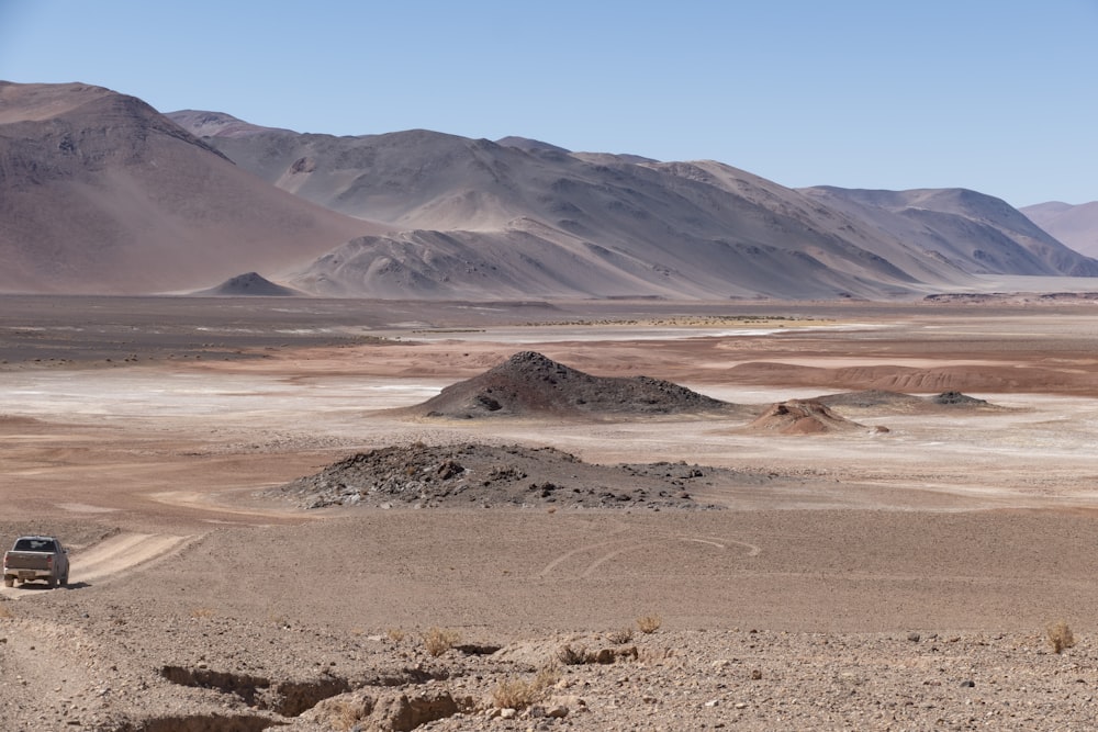 a truck driving through a desert landscape with mountains in the background