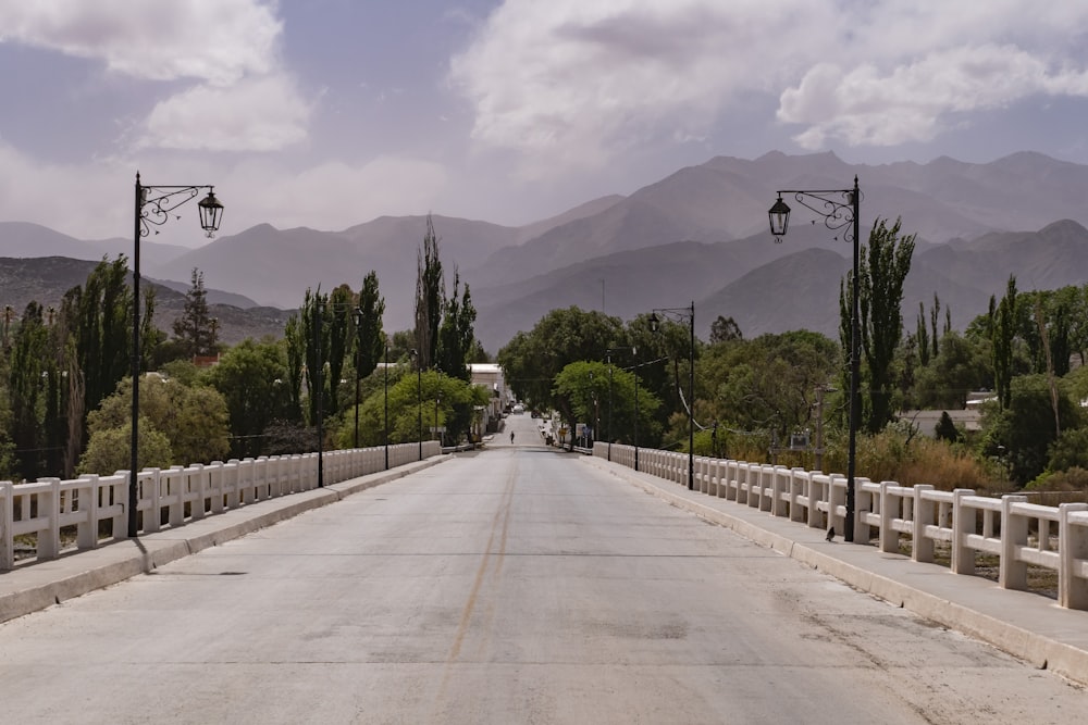 an empty street with a fence and mountains in the background