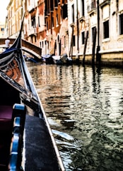 A gondola glides along a narrow canal flanked by historic, weathered buildings. The water reflects the intricate details and varied colors of the architecture, creating a harmonious and serene scene. The soft, warm light captures the essence of a quiet day in a Venetian canal.