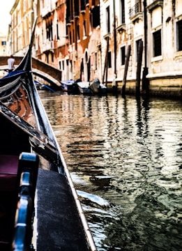 A gondola glides along a narrow canal flanked by historic, weathered buildings. The water reflects the intricate details and varied colors of the architecture, creating a harmonious and serene scene. The soft, warm light captures the essence of a quiet day in a Venetian canal.