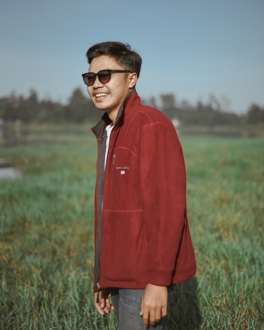 a man standing in a field wearing a red jacket