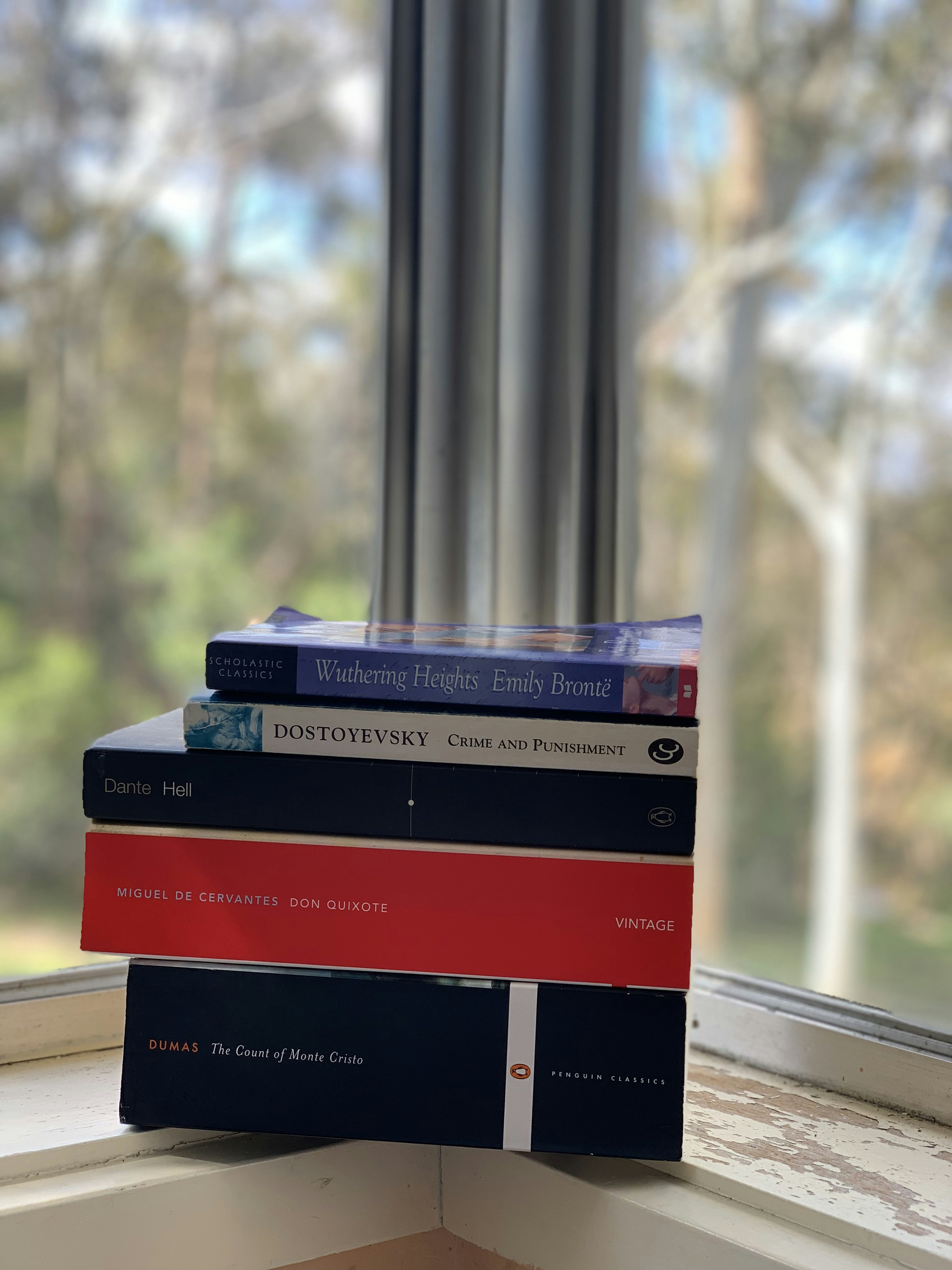 Stack of classic novels in dim library light, deep charcoal tones, atmospheric shadows