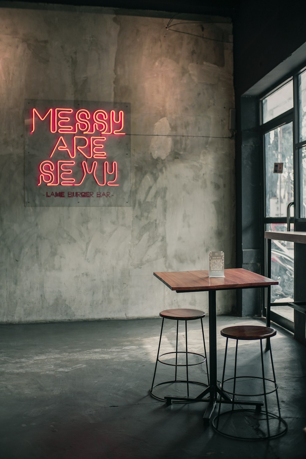 a table and two stools in front of a neon sign