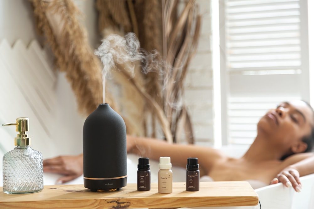 a woman laying in a bathtub next to a bottle of essential oils