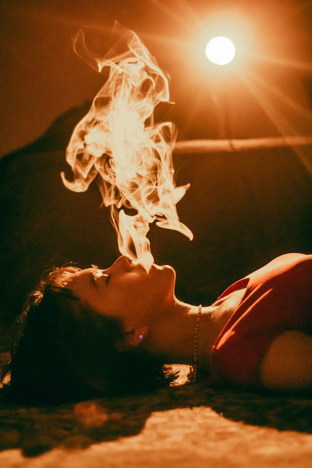 a woman laying on the ground with a fire in her mouth