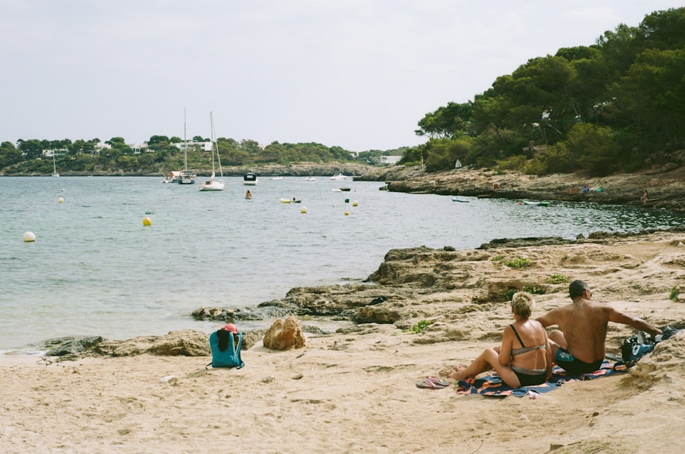 a couple of people sitting on top of a sandy beach