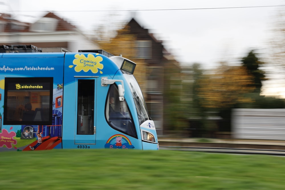 a blue bus driving down a street next to a lush green field