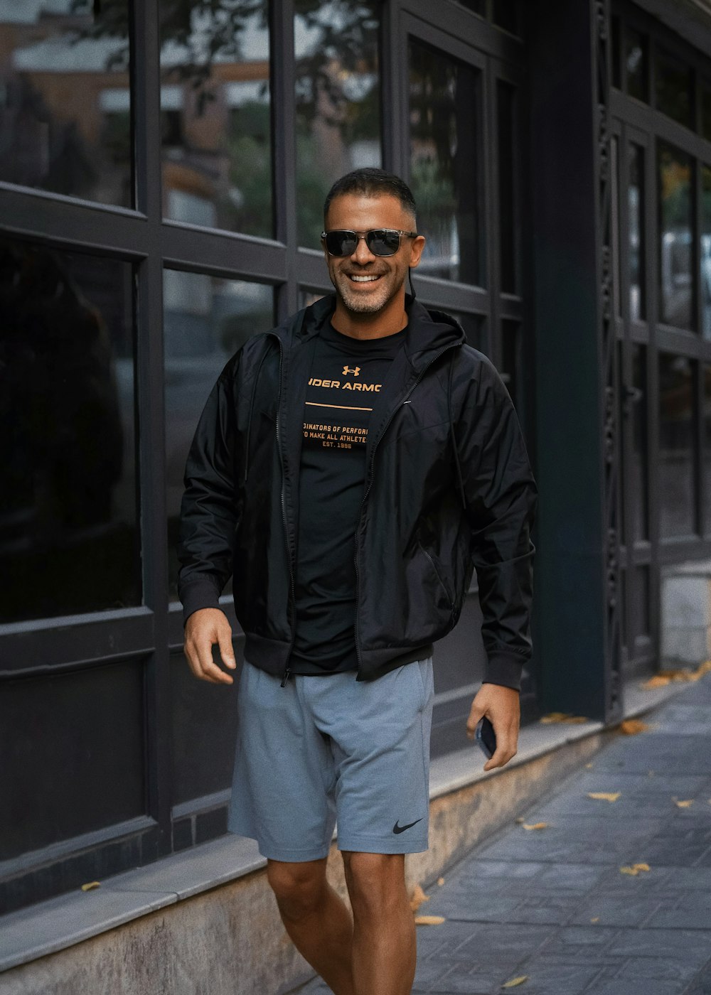 a man walking down a sidewalk wearing a black jacket
