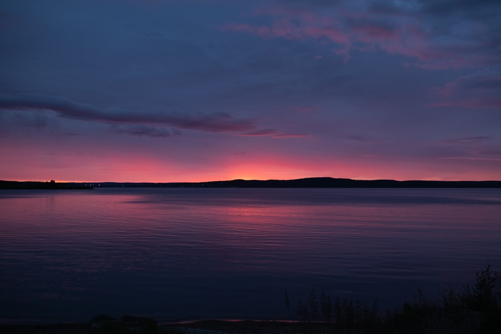 the sun is setting over a lake with a mountain in the distance