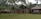 A large, rustic villa complex surrounded by lush greenery and tall palm trees. It features traditional thatched roofs and wooden structures, set against a backdrop of forested hills.