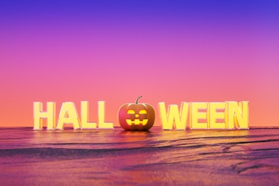 Large block letters spell out 'HALLOWEEN' with a pumpkin in place of the 'O'. The background features a gradient sky transitioning from purple to orange.